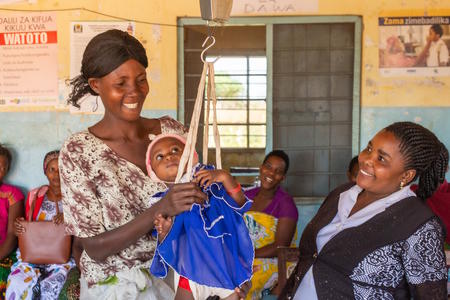 Adela, 39, with her baby Francis, 13 months, who is being weighed at Busolwa Health Centre, Nyang'hwale District, Tanzania, June, 2019.; 