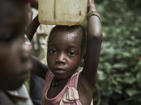 Nancy Smart, 6, carrying a container, called a 'gallon' of dirty water collected from a natural spring - the previous water source for the community of Tombohuaun. The gallon is put on her head by her mother Fatu, whom she goes with to collect water,  ...