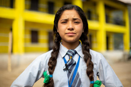 En flicka med flätor och skoluniform står med händerna i sidorna och ser bestämd ut.