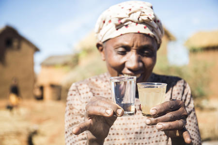 Sabine, 56, holding a side-by-side comparison of water from the newly installed tap and water from the river. Beanamamy village. Bevato  commune, Tsiroanomandidy district, Bongolava region, Madagascar, October 2018.