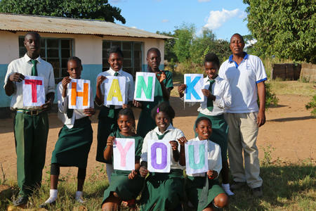 Pupils and their Head Teacher display a 'Thank you' sign for the piped water system that was recently installed at their school.